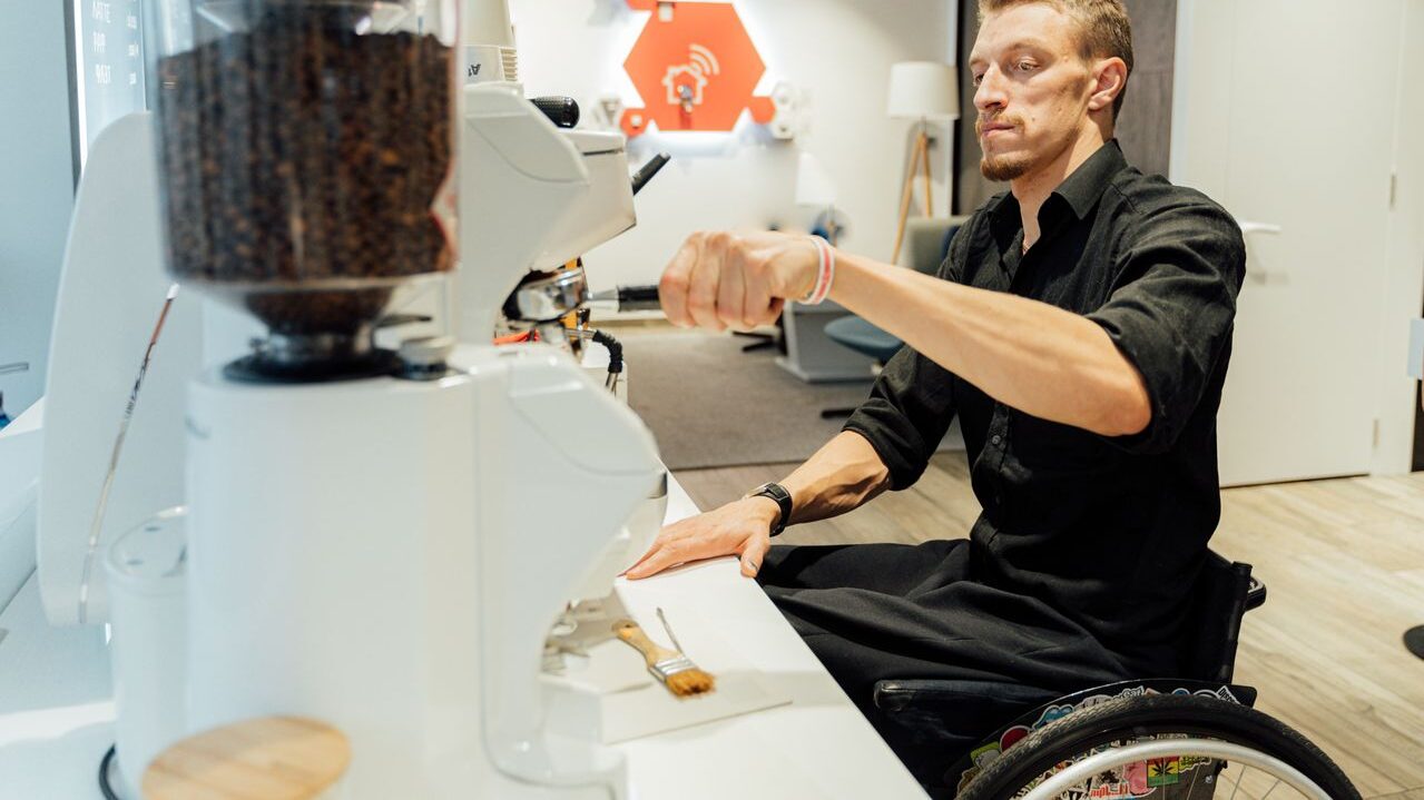 Young man is making coffee at coffee shop. He is an employee in a wheelchair