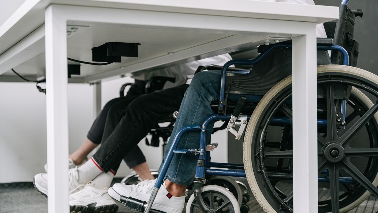 Under the table look - meeting, employees with and without disabilities - one employee is using wheelchair, another is sitting on the chair