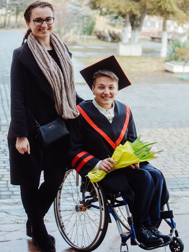 Young lady standing next to a young men in a wheelchair who've just graduated and wearing graduation gown