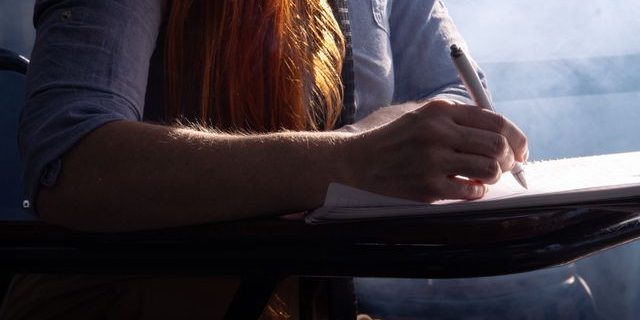 A red head lady sitting and writing by hand